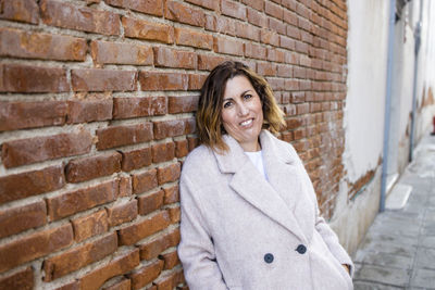 Portrait of young woman standing against brick wall