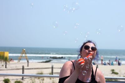 Young woman blowing bubbles at beach against sky