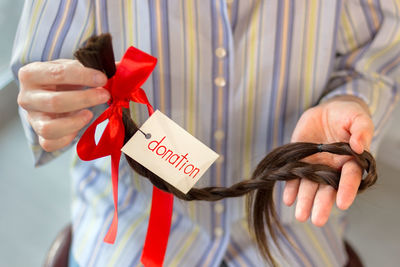 Long cut braid with tag and red ribbon bow in woman hands, donation of haircut, faceless concept