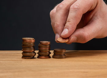 Cropped image of hand holding coins on table against black background