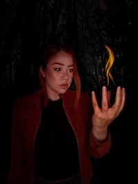 Portrait of young woman standing against black background