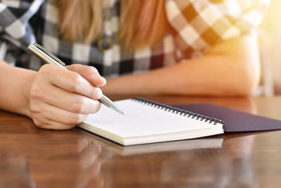 Midsection of woman writing in book at table