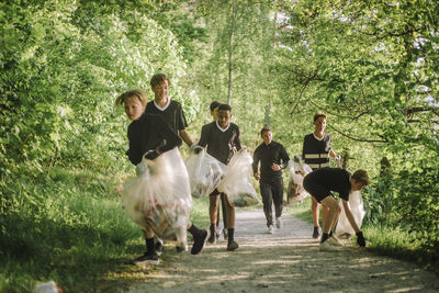 Boys and coach plogging on footpath amidst green plants