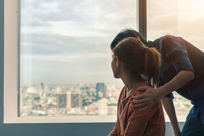 Midsection of woman standing by window against cityscape