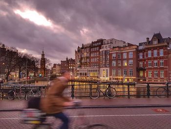 Blurred motion of man riding on bicycle in city during sunset