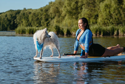 Woman doing stretching while paddleboarding with her pet on lake, japanese spitz stand on sup board
