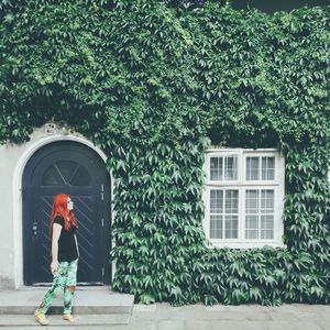 Full length of woman standing against house covered with ivy leaves