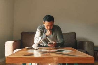 Man using smart phone while sitting on sofa at home