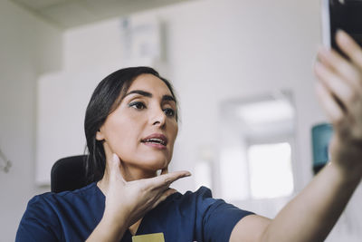 Female nurse doing online consultation through smart phone at hospital