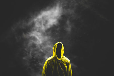 Silhouette man wearing yellow raincoat standing against black background