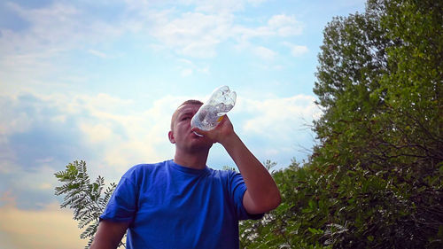 Man looking away while drinking water from bottle against sky