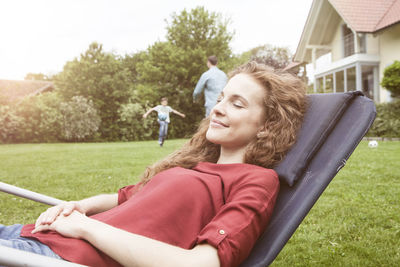 Woman relaxing in deckchair in garden with family in background