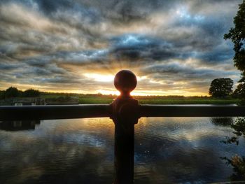 Side view of man overlooking calm lake at sunset