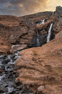 Low angle view of hengifoss waterfall amidst cliffs against sky during sunset