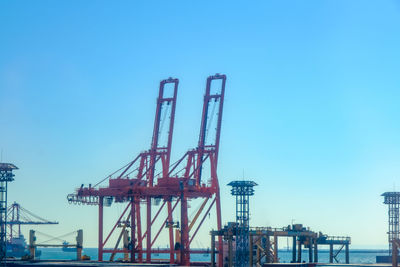 Cranes at commercial dock against clear sky