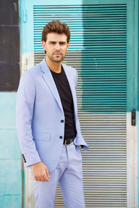 Portrait of young businessman standing against wall