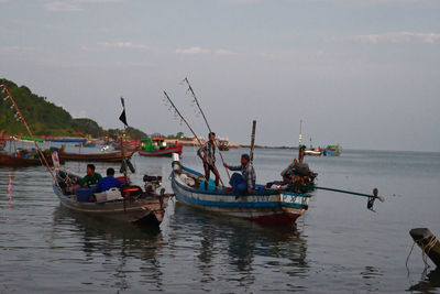 People on fishing boats in sea against sky