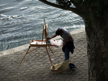 An artist painting under a tree by the river