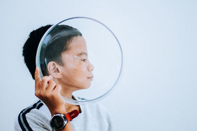 Close-up of boy holding glass bowl against white background