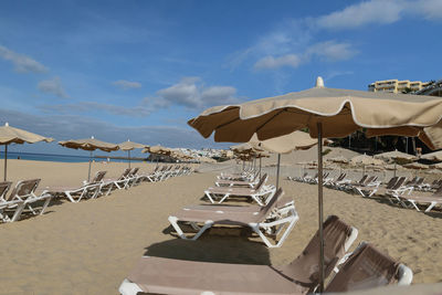 Lounge chairs and parasols on beach against sky