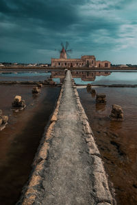 Empty footpath leading towards traditional windmill against cloudy sky