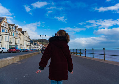 Rear view of girl walking on promenade against sky