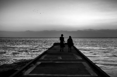 People in sea against sky during sunset