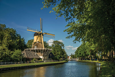 Traditional windmill by river against sky