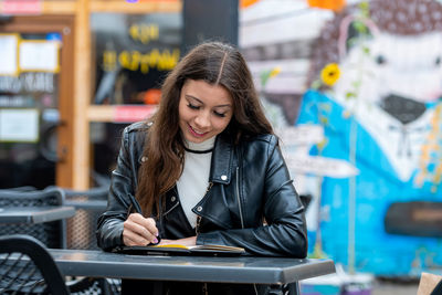 Smiling woman writing in diary while sitting at cafe