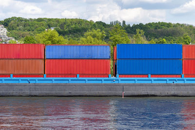 A barge carrying many containers on the rhine in western germany, trees and buildings in the back