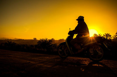 Silhouette man riding bicycle on road against sky during sunset