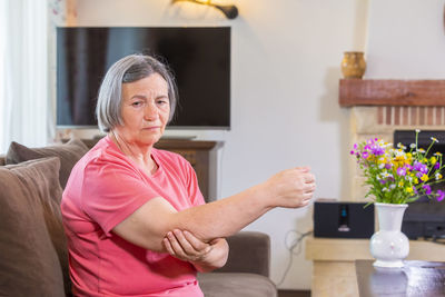 Woman with elbow pain sitting on sofa at home