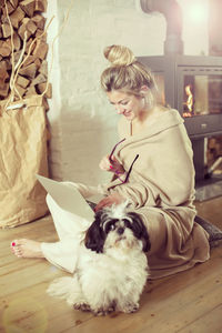 Smiling young woman using laptop while sitting with dog at home