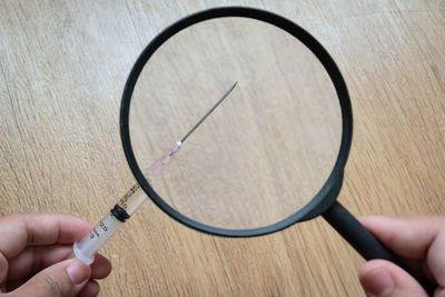 Cropped image of hand holding syringe and magnifying glass