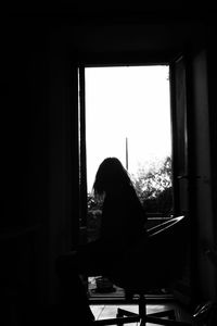 Rear view of silhouette woman sitting at home