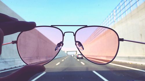 Cropped hand holding sunglasses against car windshield with sky in background