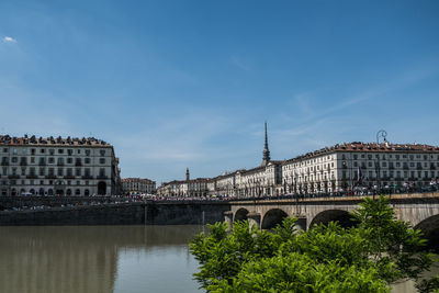 Bridge over river by buildings against sky