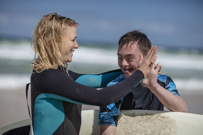 Happy teenage boy with down syndrome and woman with surfboard on beach