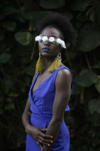 Woman wearing flowers over eyes while standing against plants