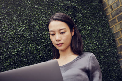 Businesswoman working on laptop in front of green wall