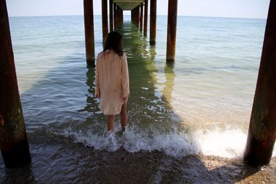 Rear view of woman walking on sea shore below pier