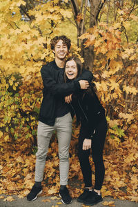 Full length of happy teenage friends smiling against trees in autumn