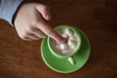 Cropped hand touching sugar cubes in cup at table