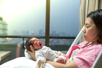 Mother holding newborn baby while lying on bed