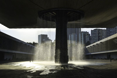 Fountain in city by buildings against sky