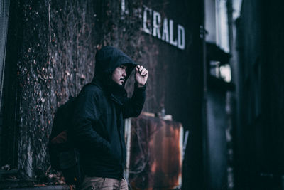 Side view of man wearing hat standing against wall