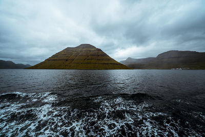 Scenic view of sea by mountain against sky