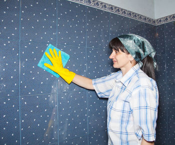 Woman cleaning tiled wall at home