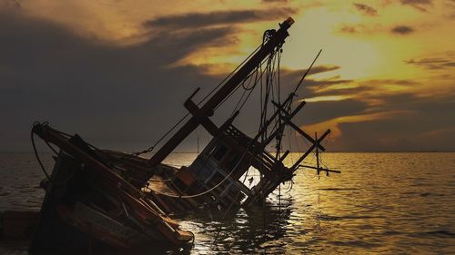 Shipwreck in sea against sky during sunset