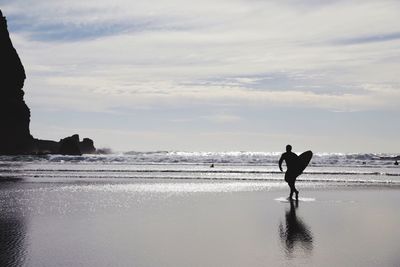 Silhouette man walking on beach against sky